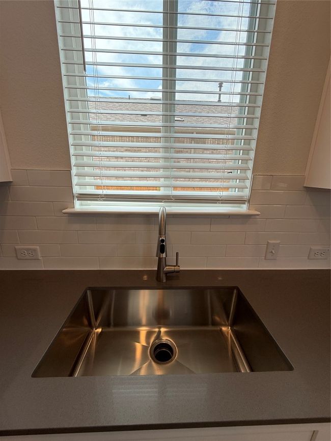 Kitchen view of a sink, backsplash, white cabinets, and dark countertops | Image 17
