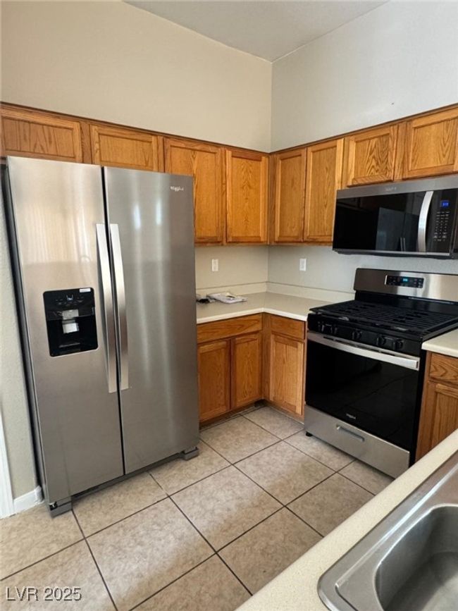 Kitchen with light countertops, light tile patterned flooring, appliances with stainless steel finishes, and brown cabinetry | Image 7