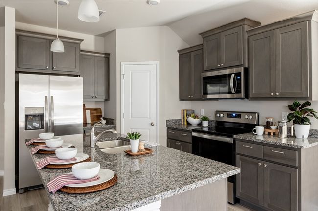 Kitchen with a kitchen island with sink, decorative light fixtures, stainless steel appliances, light wood finished floors, and light stone countertops | Image 6
