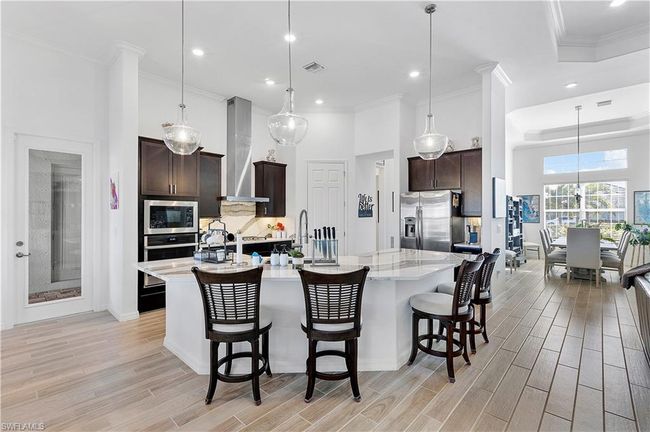 Kitchen featuring tasteful backsplash, stainless steel appliances, dark brown cabinetry, wall chimney range hood, and wood tiled floor | Image 35
