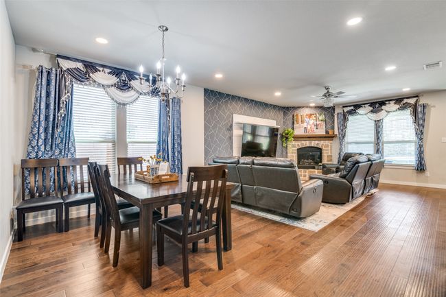 Dining space with a chandelier, a stone fireplace, a ceiling fan, recessed lighting, and wood finished floors | Image 7