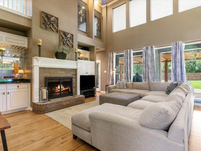 Living area featuring light wood-style flooring, a high ceiling, and a fireplace | Image 14