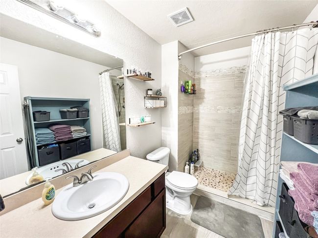 Full bathroom with vanity, a tile shower, toilet, wood finished floors, and a textured wall | Image 4