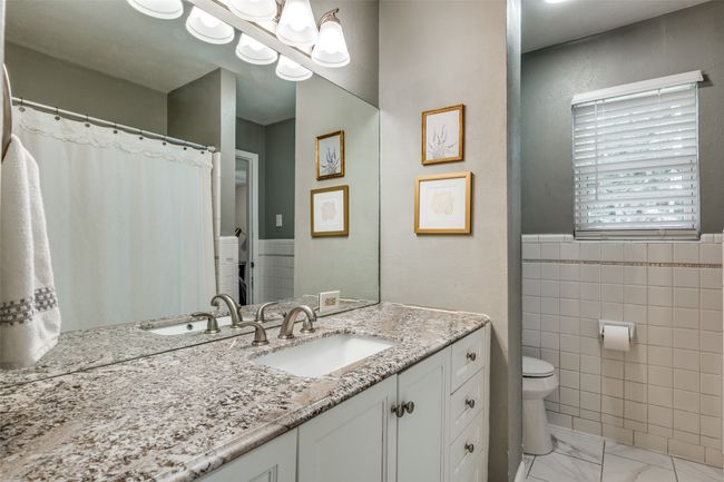 Full bath with vanity, marble look tile flooring, tile walls, and a chandelier | Image 26