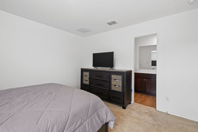 Bedroom with connected bathroom, light carpet, and visible vents | Image 11