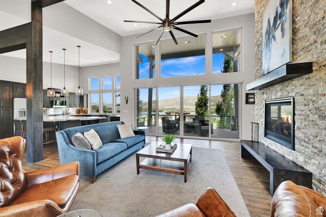 Living room featuring ceiling fan, a towering ceiling, wood finished floors, a stone fireplace, and recessed lighting | Image 14
