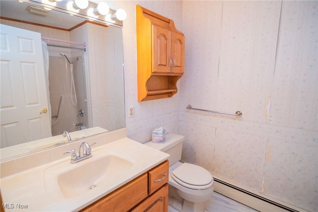 Bathroom with baseboard heating, vanity, toilet, wallpapered walls, and bathtub / shower combination | Image 13