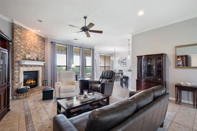 Living area featuring a ceiling fan, crown molding, a brick fireplace, light tile patterned flooring, and recessed lighting | Image 4