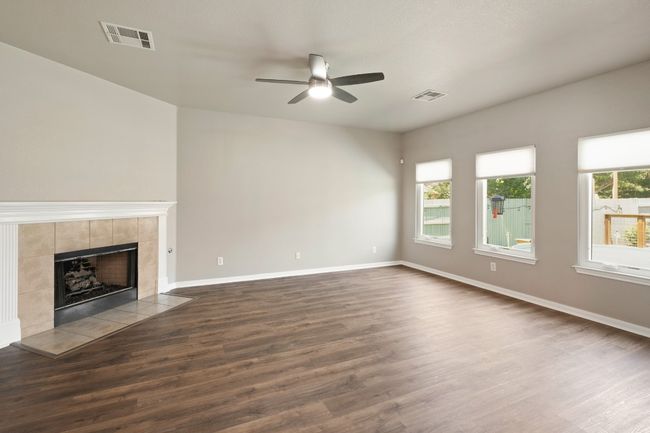 Unfurnished living room featuring a ceiling fan, dark wood-type flooring, a tile fireplace, and baseboards | Image 7
