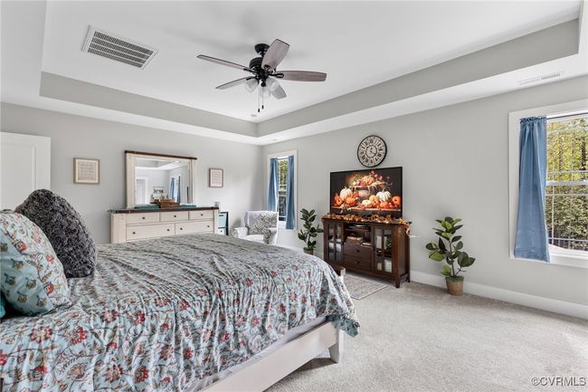 Carpeted bedroom featuring a ceiling fan, baseboards, visible vents, and a raised ceiling | Image 30