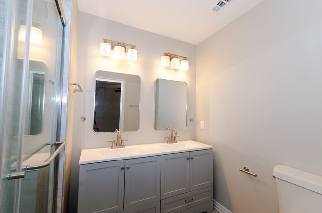 Bathroom with visible vents, a stall shower, toilet, and a sink | Image 12