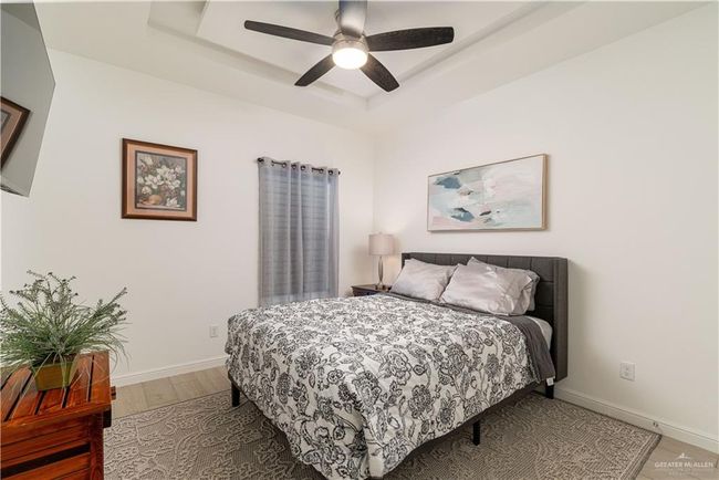 Bedroom featuring baseboards, light wood-style flooring, a raised ceiling, and ceiling fan | Image 12