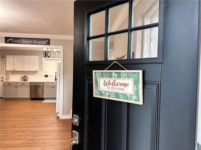 Details featuring white cabinets, light wood-type flooring, crown molding, a textured ceiling, and stainless steel dishwasher | Image 1