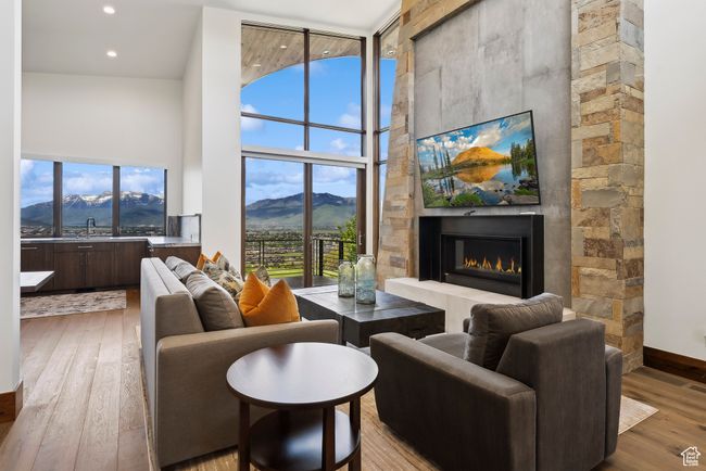 Living area featuring a high ceiling, a glass covered fireplace, light wood finished floors, baseboards, and recessed lighting | Image 88