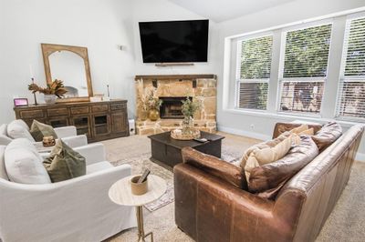 Carpeted living room featuring a stone fireplace, ceiling fan, and lots of natural light. | Image 3