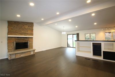 Unfurnished living room with an inviting chandelier, a stone fireplace, lofted ceiling with beams, and dark hardwood / wood-style floors | Image 3