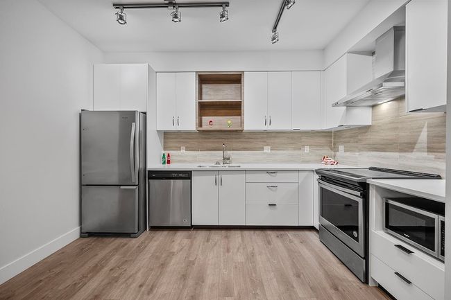 Kitchen with stainless steel appliances, wall chimney range hood, light countertops, and open shelves | Image 13