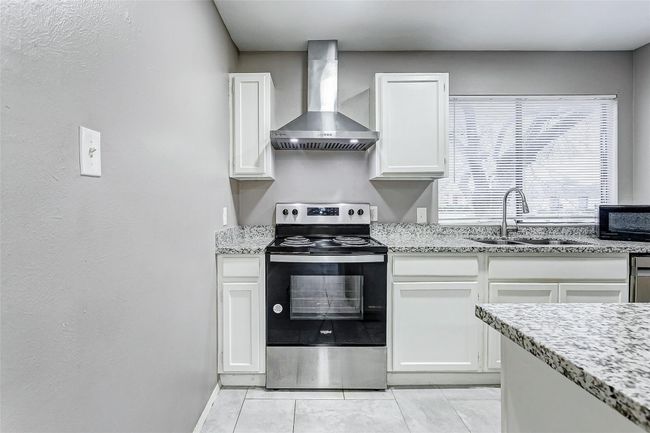 The sleek kitchen boasts modern updates with granite countertops, stainless steel appliances, and white cabinetry. A raised breakfast bar overlooks the open living area, making it easy to entertain or share meals. Bright recessed lighting ensures the space feels light and welcoming, while the open layout ties the kitchen seamlessly to the rest of the home. | Image 7