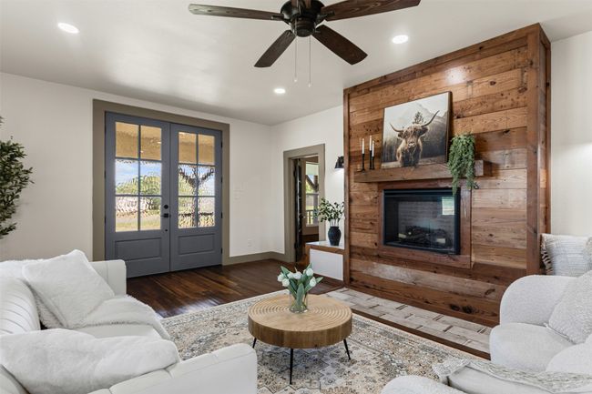 Living room with french doors, wood finished floors, recessed lighting, a large fireplace, and ceiling fan | Image 10