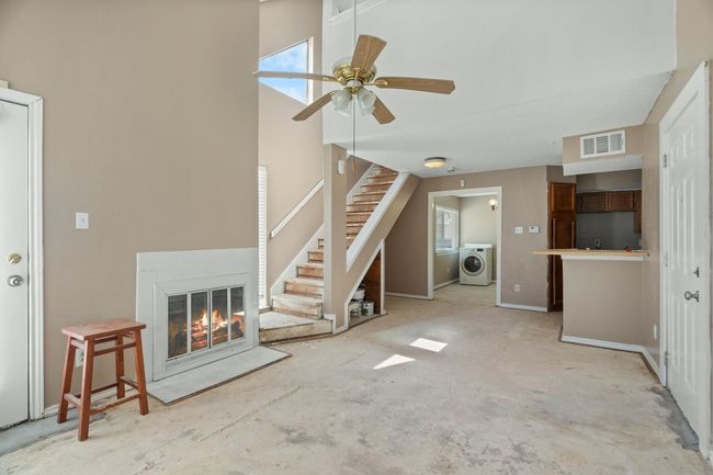 Unfurnished living room featuring washer / clothes dryer, stairway, a ceiling fan, a glass covered fireplace, and plenty of natural light | Image 4