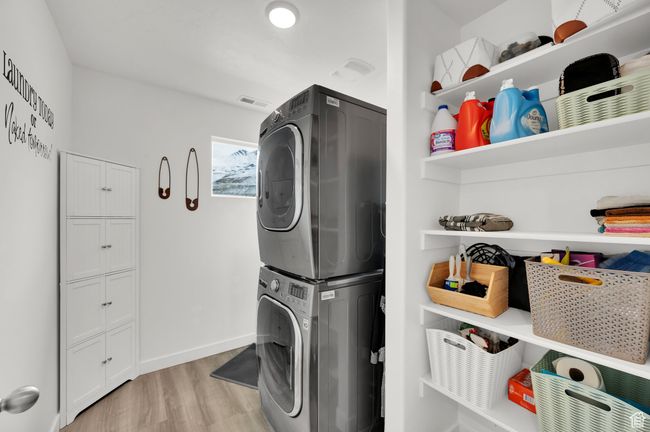 Clothes washing area featuring baseboards, light wood-style flooring, laundry area, and stacked washing maching and dryer | Image 16