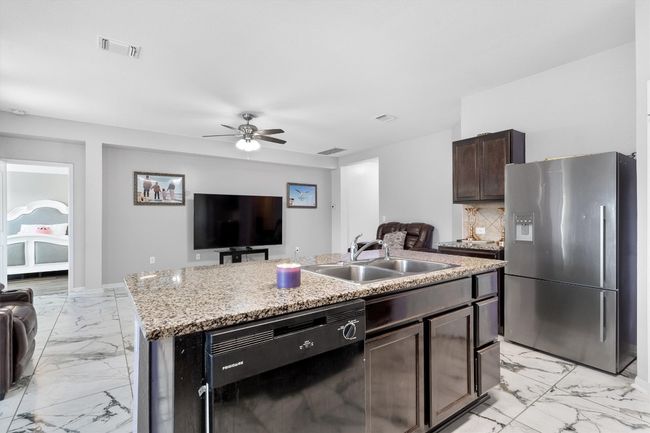 Kitchen with stainless steel fridge with ice dispenser, dishwasher, a sink, light marble finish flooring, and open floor plan | Image 11