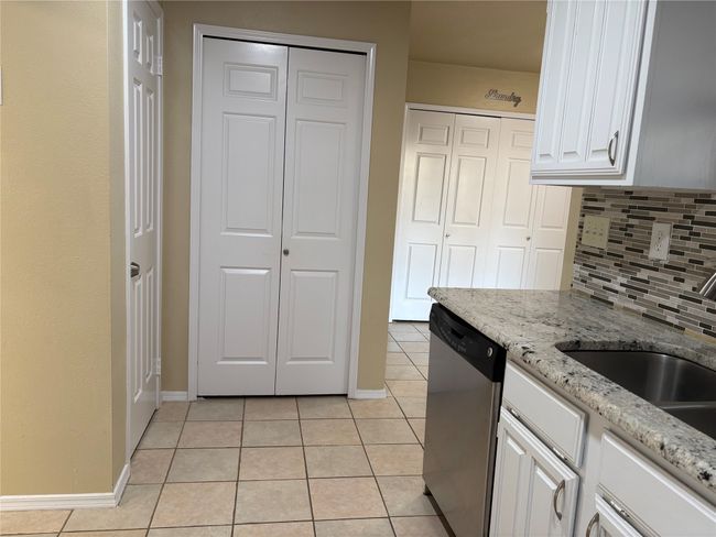 Kitchen with light tile patterned flooring, white cabinets, backsplash, and stainless steel dishwasher | Image 9