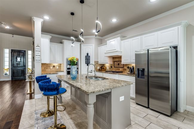 Kitchen featuring stainless steel appliances, premium range hood, crown molding, light stone countertops, and white cabinets | Image 7