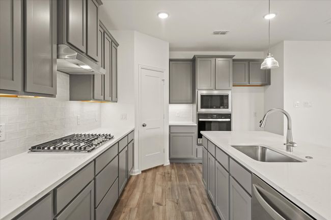 Kitchen featuring appliances with stainless steel finishes, under cabinet range hood, dark wood-style floors, pendant lighting, and backsplash | Image 17