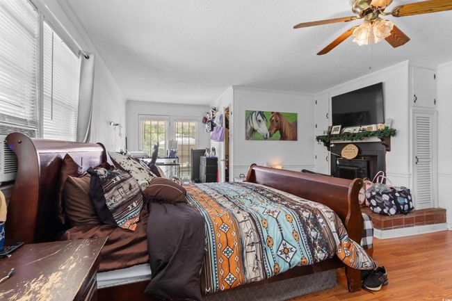 Bedroom featuring a textured ceiling, wood finished floors, ceiling fan, a fireplace, and ornamental molding | Image 23
