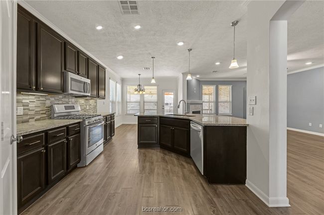 Kitchen featuring sink, light stone counters, decorative light fixtures, stainless steel appliances, and decorative backsplash | Image 6