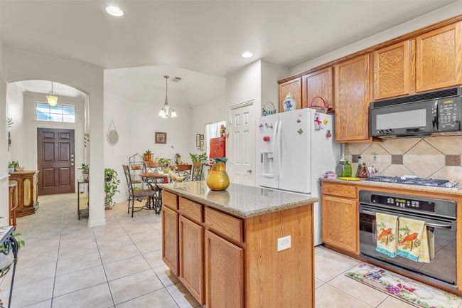 Kitchen featuring black appliances, arched walkways, light tile patterned floors, backsplash, and a center island | Image 22