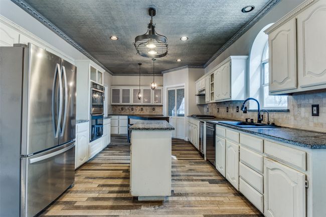 Kitchen with a sink, white cabinets, a kitchen island, and stainless steel appliances | Image 12