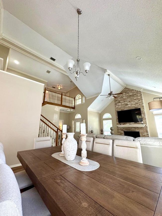 Dining space with vaulted ceiling, a fireplace, stairway, visible vents, and ceiling fan with notable chandelier | Image 15