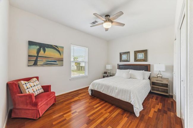 This bedroom features warm wood flooring, a cozy bed with neutral bedding, and a stylish ceiling fan. | Image 22
