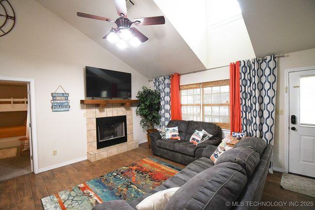 Living room featuring a ceiling fan, high vaulted ceiling, wood finished floors, a fireplace, and baseboards | Image 4