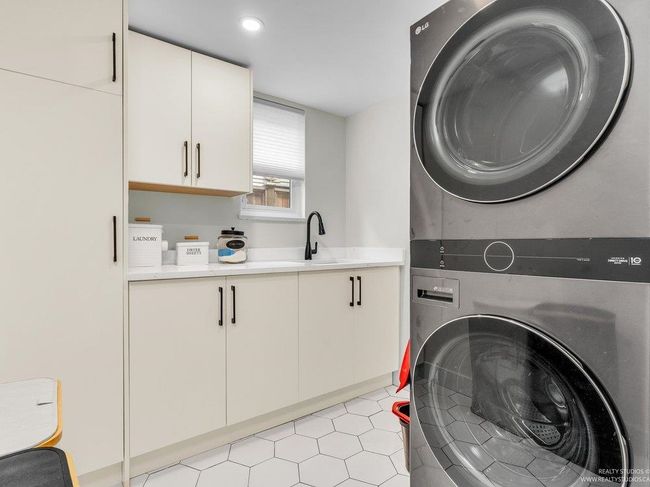 Full Laundry Room with sink, a folding counter, a window, loads of cabinetry for storage and a stacked washer dryer. Adjacent to this is the Hot water on demand system as well as the furnace and its newly installed Air con system for the upper floor. | Image 36