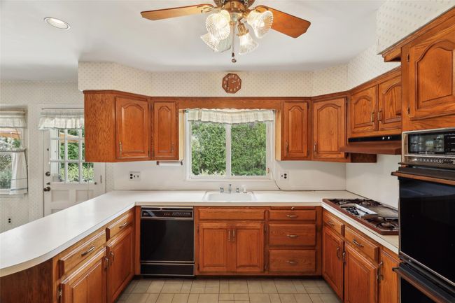 Kitchen with black appliances, a ceiling fan, a sink, and wallpapered walls | Image 7