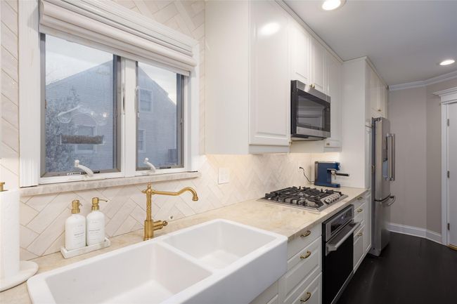 Kitchen with white cabinets, stainless steel appliances, light countertops, a sink, and decorative backsplash | Image 20