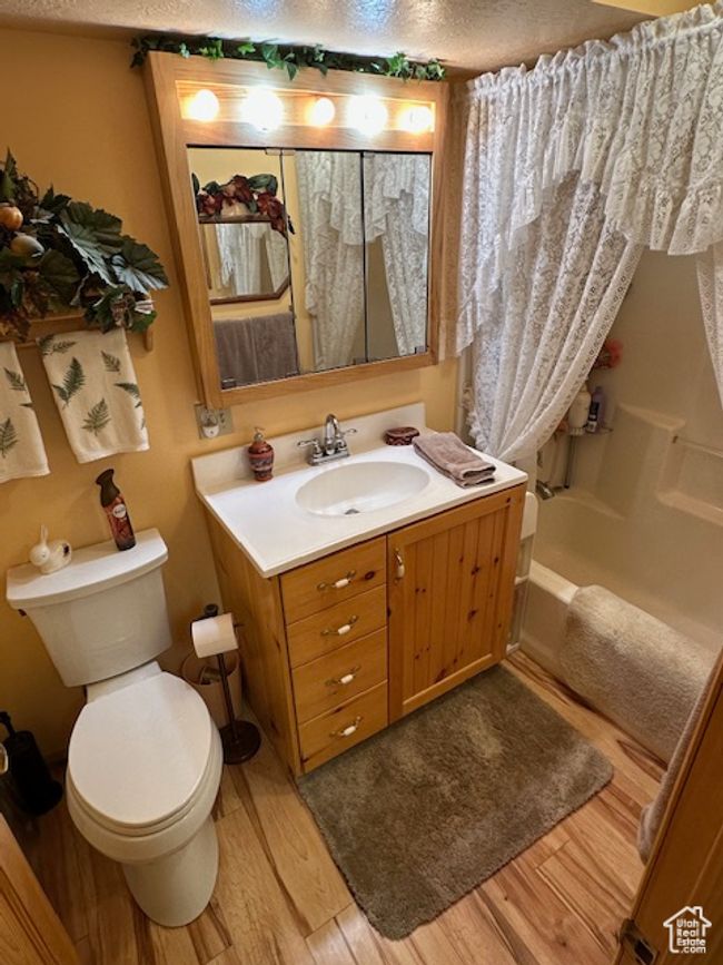 Full bath featuring shower / tub combo, toilet, a textured ceiling, vanity, and wood finished floors | Image 14
