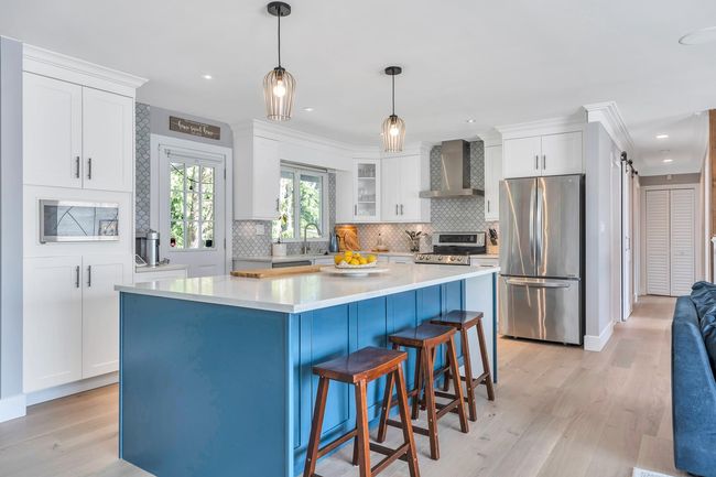 Kitchen featuring tasteful backsplash, white cabinetry, stainless steel appliances, and wall chimney exhaust hood | Image 7