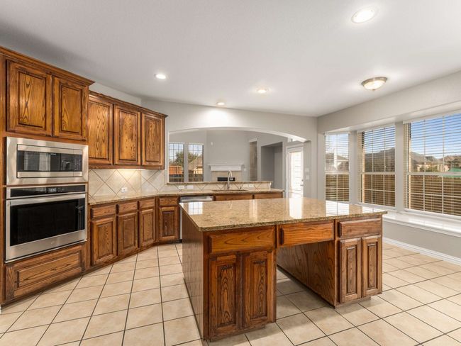 Kitchen with backsplash, a center island, light tile patterned flooring, arched walkways, and stainless steel appliances | Image 13