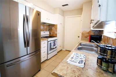 Kitchen featuring white gas range oven, sink, white cabinetry, stainless steel refrigerator, and decorative backsplash | Image 2