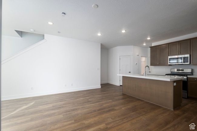 Kitchen with a sink, light countertops, dark wood-style flooring, appliances with stainless steel finishes, and a kitchen island with sink | Image 9