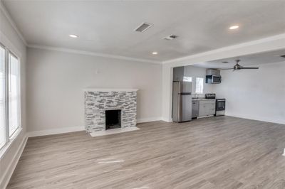 Unfurnished living room featuring ceiling fan, light wood-type flooring, a fireplace, crown molding, and sink | Image 3