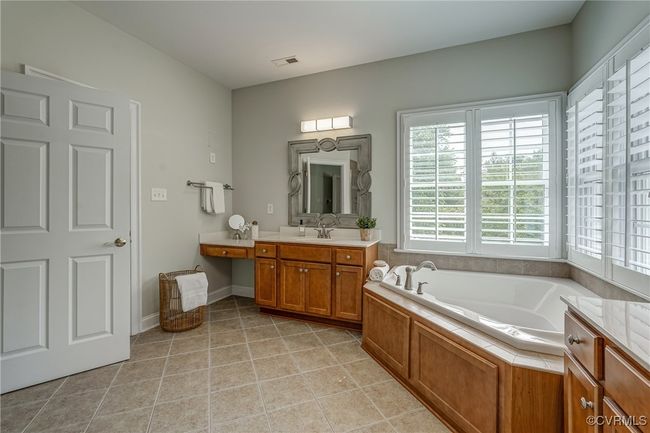 Elegant primary bath with a double vanity, soaking tub, tile floors, and plantation shutters—designed for both relaxation and refined detail. | Image 37