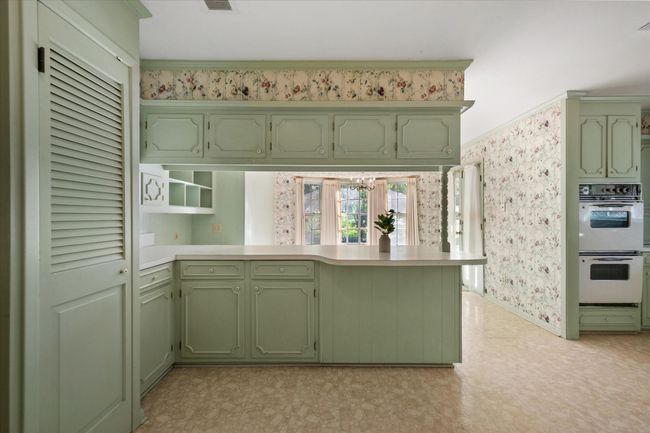 Kitchen with green cabinetry, double oven, wallpapered walls, a peninsula, and light countertops | Image 10