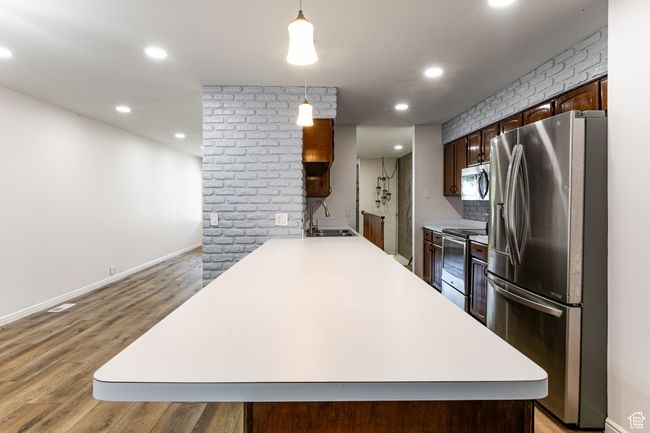 Kitchen featuring stainless steel appliances, a sink, light countertops, light wood-type flooring, and recessed lighting | Image 11