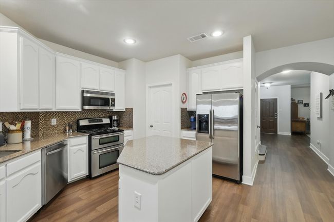 Kitchen featuring appliances with stainless steel finishes, arched walkways, white cabinets, tasteful backsplash, and recessed lighting | Image 15