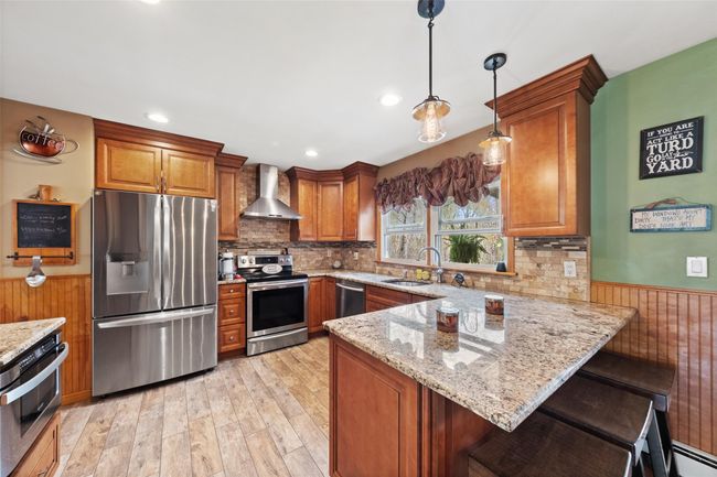 Kitchen featuring brown cabinets, wall chimney range hood, a peninsula, and stainless steel appliances | Image 8